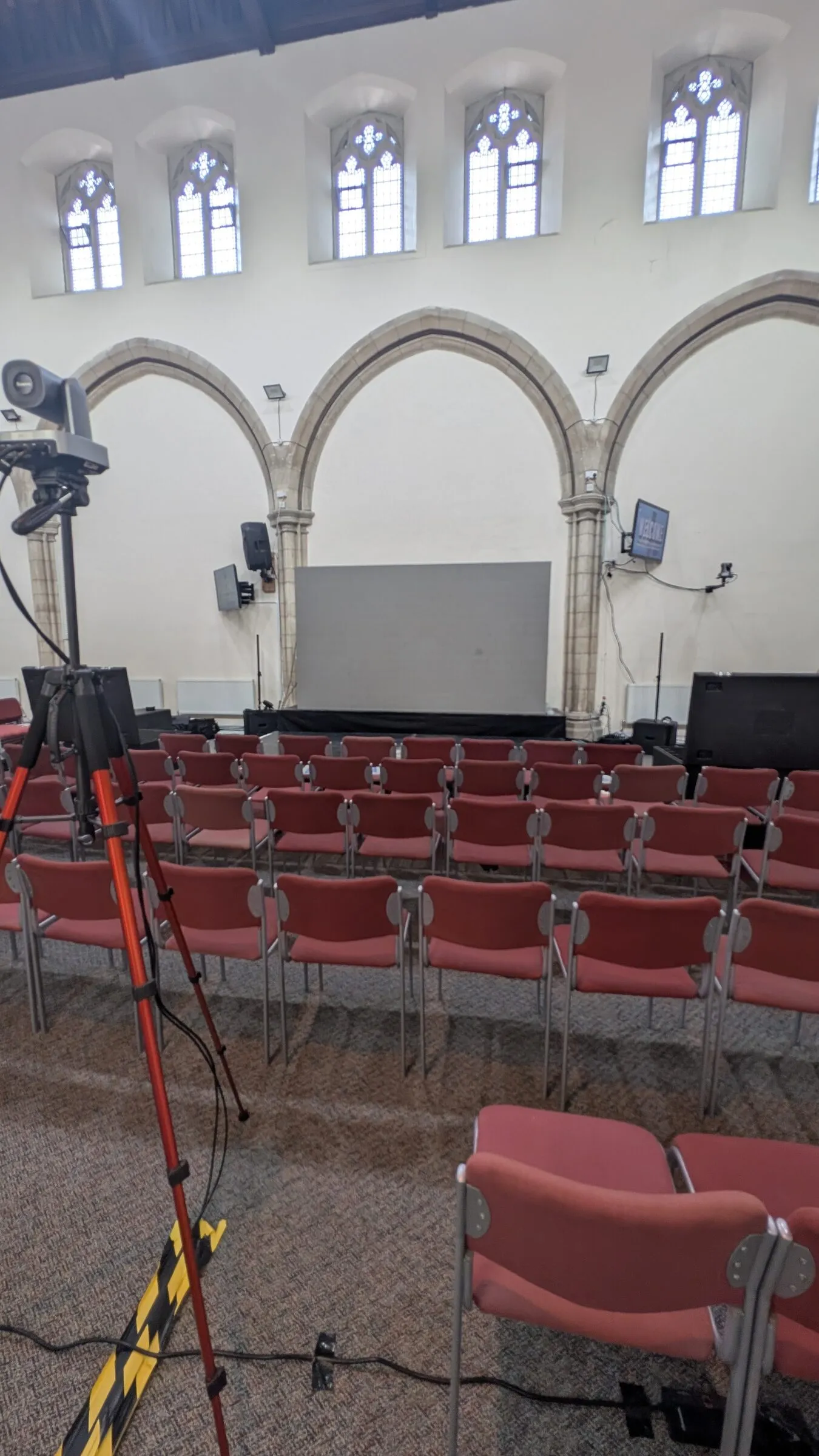 Rows of chairs facing the stage and screen at Full Gospel Revival Centre, with a camera on a tripod in the foreground.